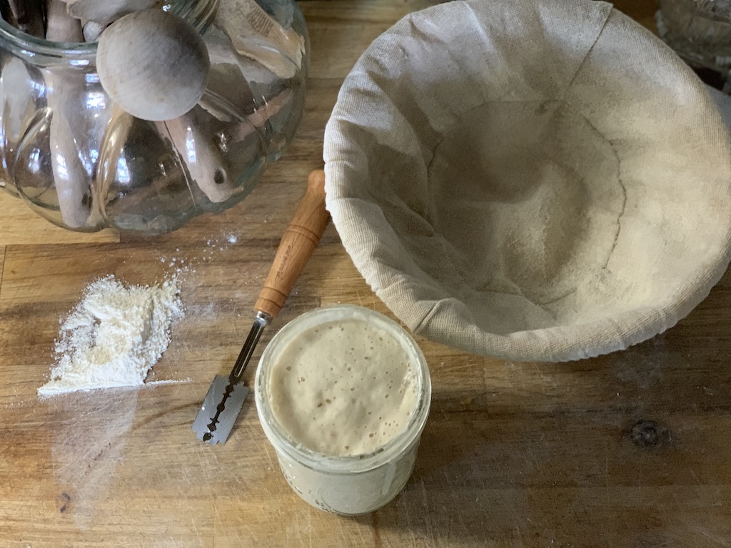 Banneton Proofing Bowl, Bubbly Sourdough Starter, and Bread Lame on Butcher Block cutting board