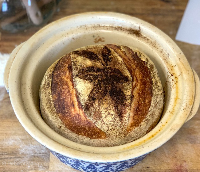 Baked sourdough bread inside ceramic crock resting on a cutting board.