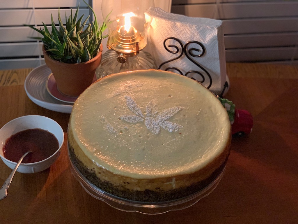 Classic New York Style Cheesecake topped with stenciled powdered sugar poinsettia flower, displayed on dining table with strawberry and chocolate ganache sauces on side.