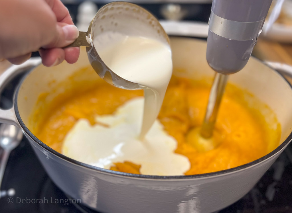 Pouring heavy cream into pureed butternut squash soup.