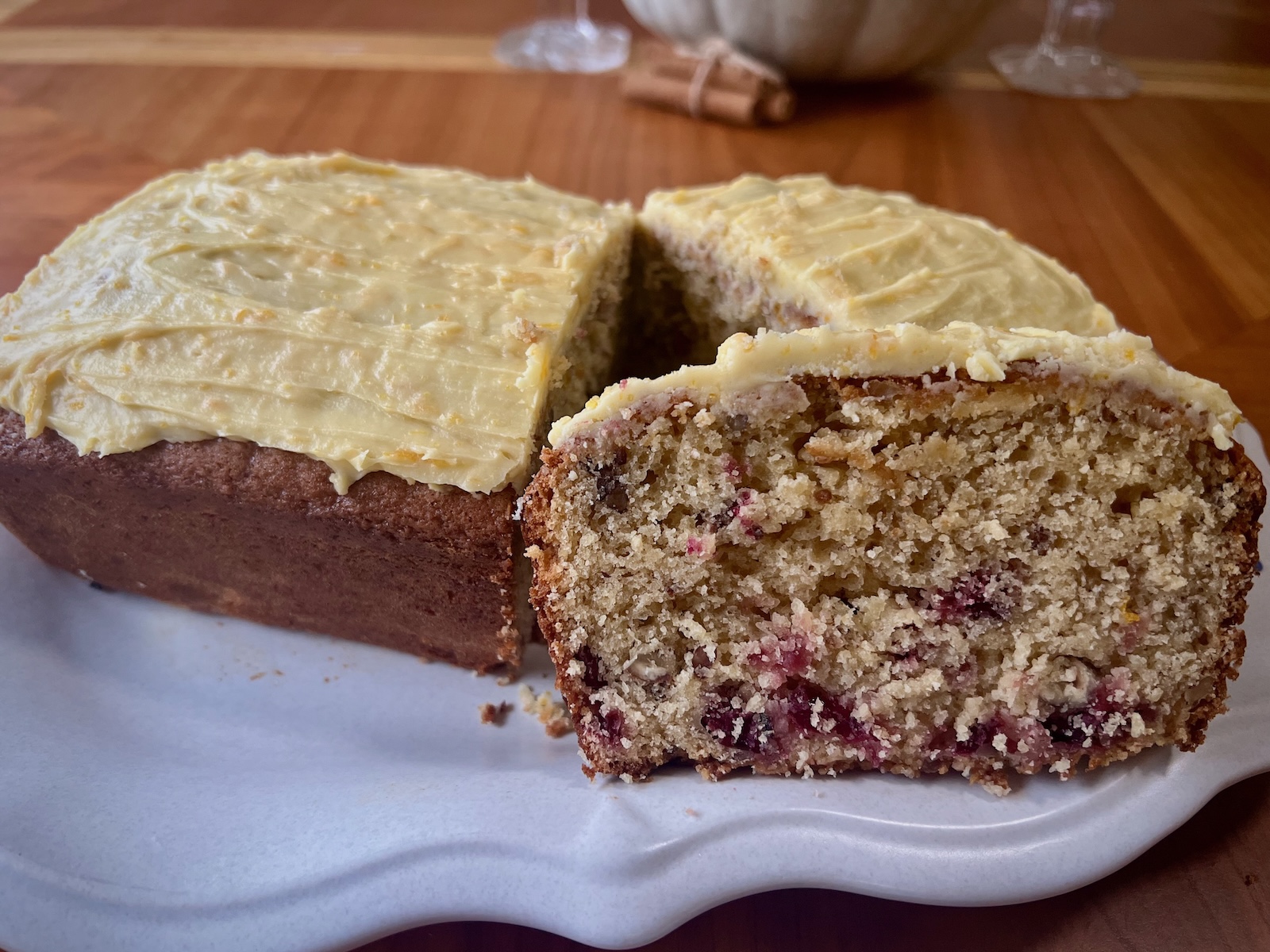 Cranberry orange sourdough loaf with orange frosting, sliced to show cranberries and pecans inside.