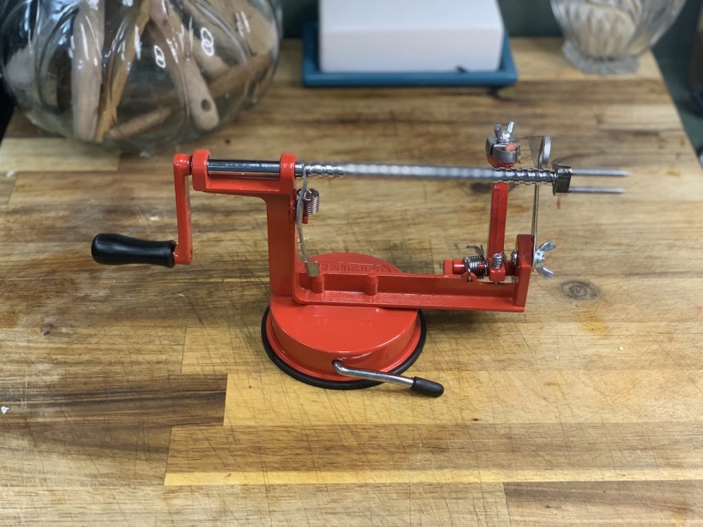 Red crank apple peeler on a wooden cutting board