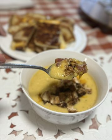 Butternut Squash Soup scooped on a spoon with bacon and grilled chicken. Grilled cheese in the background
