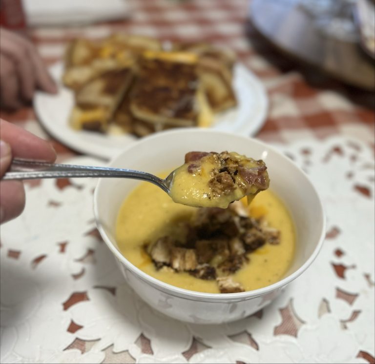 Butternut Squash Soup scooped on a spoon with bacon and grilled chicken. Grilled cheese in the background