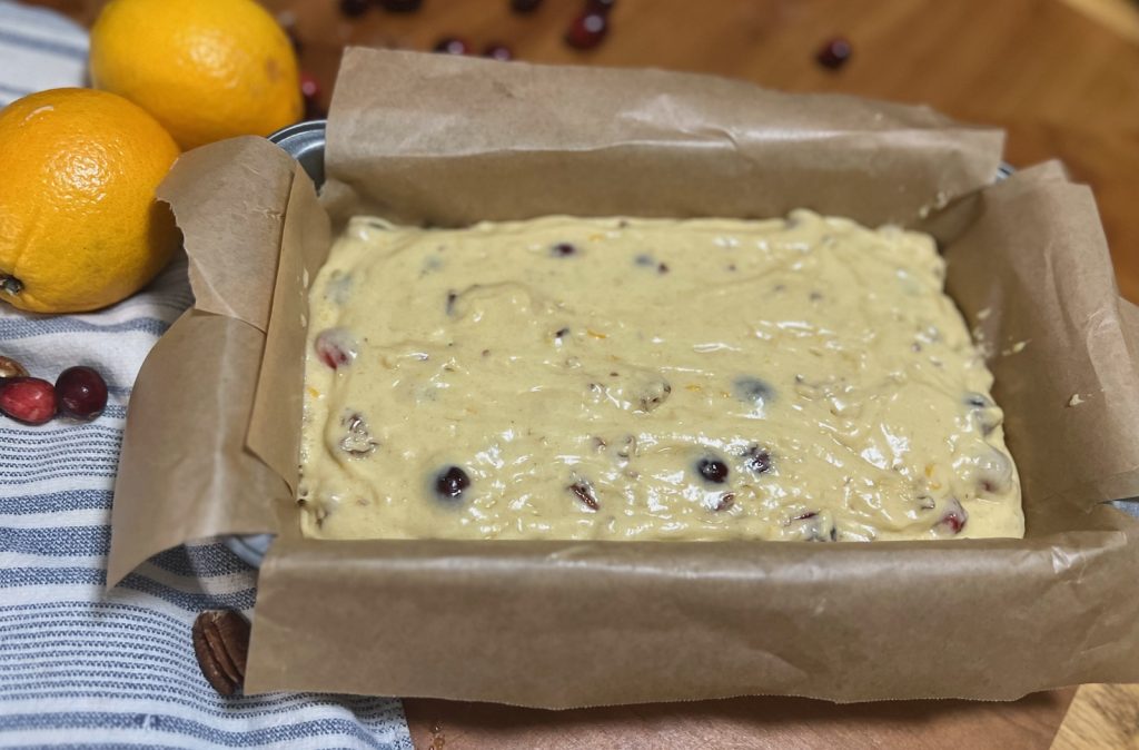 Canberry pecan sourdough bread batter spread in a parchment-lined loaf pan.