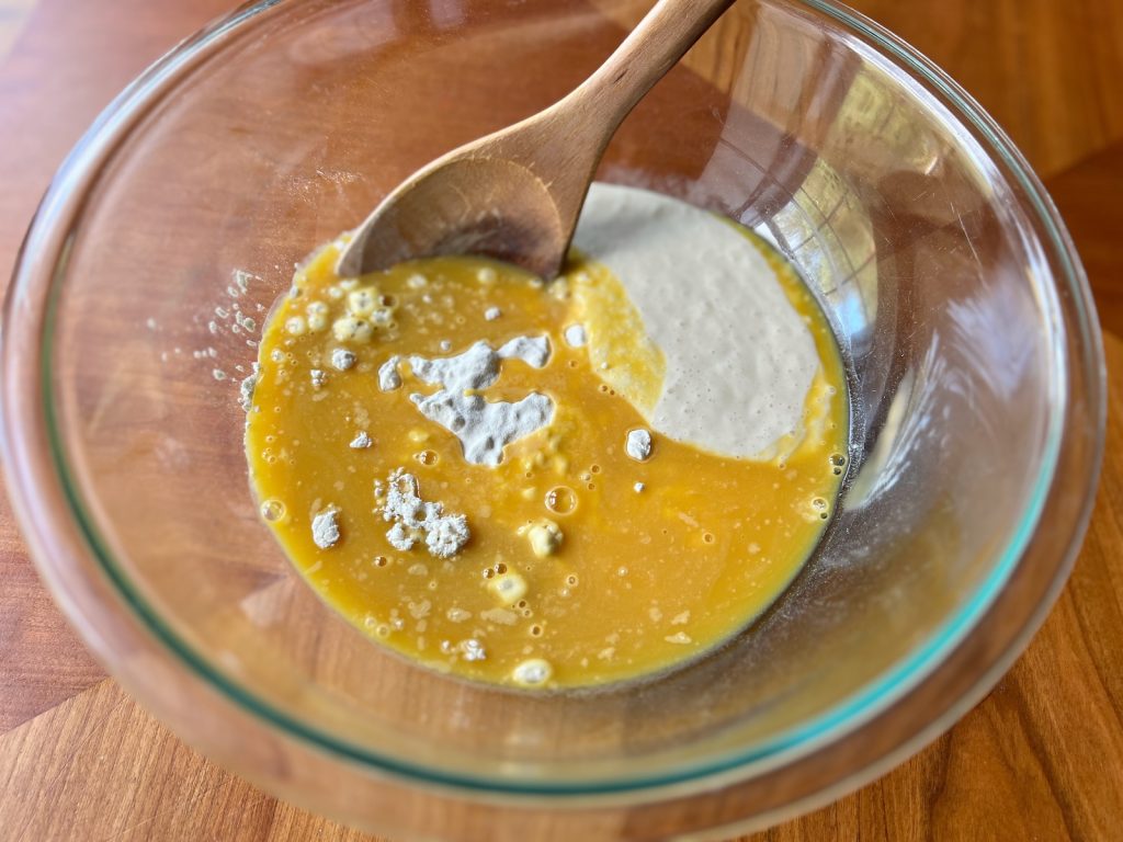 Sourdough starter and orange juice concentrate added to flour in a glass mixing bowl.