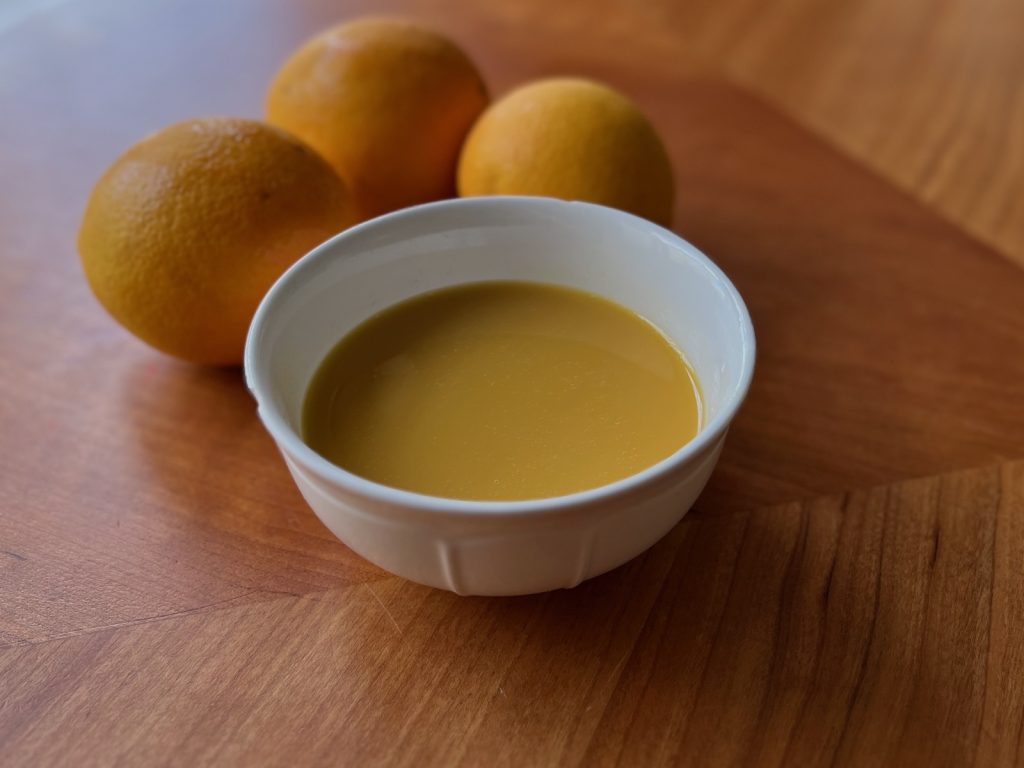 Frozen orange juice concentrate, thawed, in a white bowl with fresh oranges in the background.