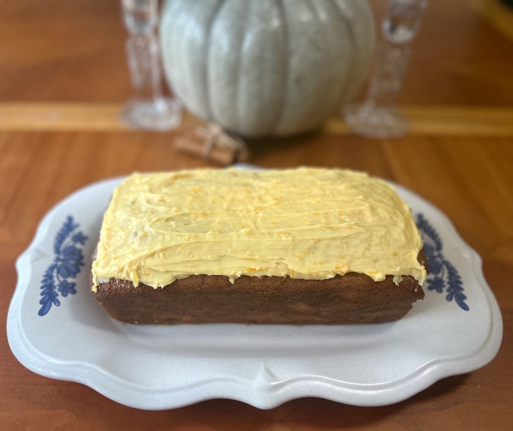 Whole cranberry orange sourdough loaf topped with orange frosting on a blue-and-white serving platter.