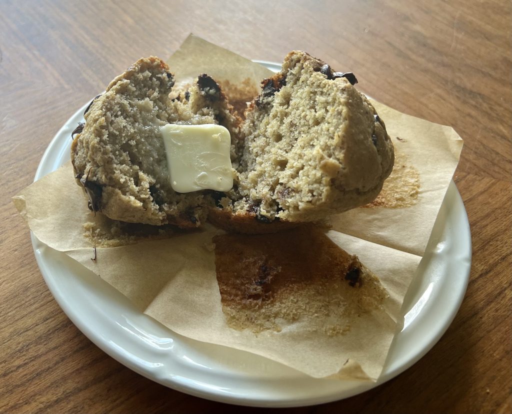 Fresh-milled banana chocolate chip muffin split open with butter melting into the warm crumb