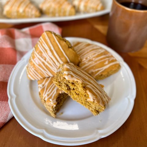Fresh-Milled Pumpkin Sourdough Discard Scones Glazed pumpkin sourdough discard scones on a white plate with coffee and a rust-colored checkered cloth.