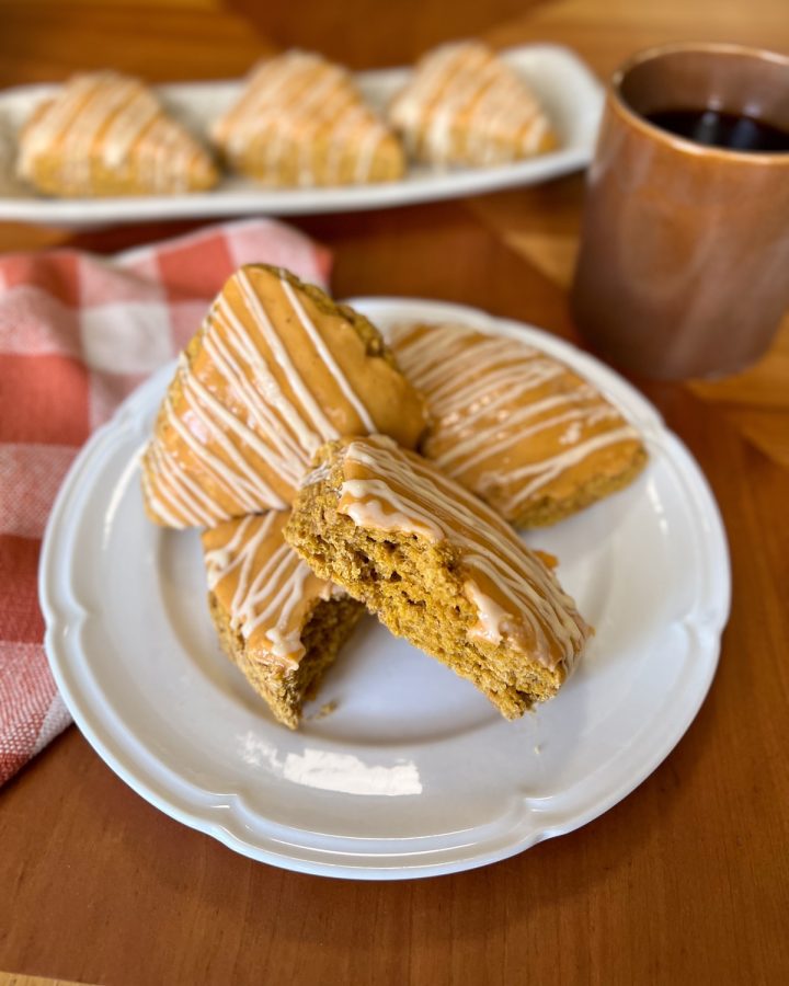 Glazed pumpkin sourdough discard scones on a white plate with coffee and a rust-colored checkered cloth.