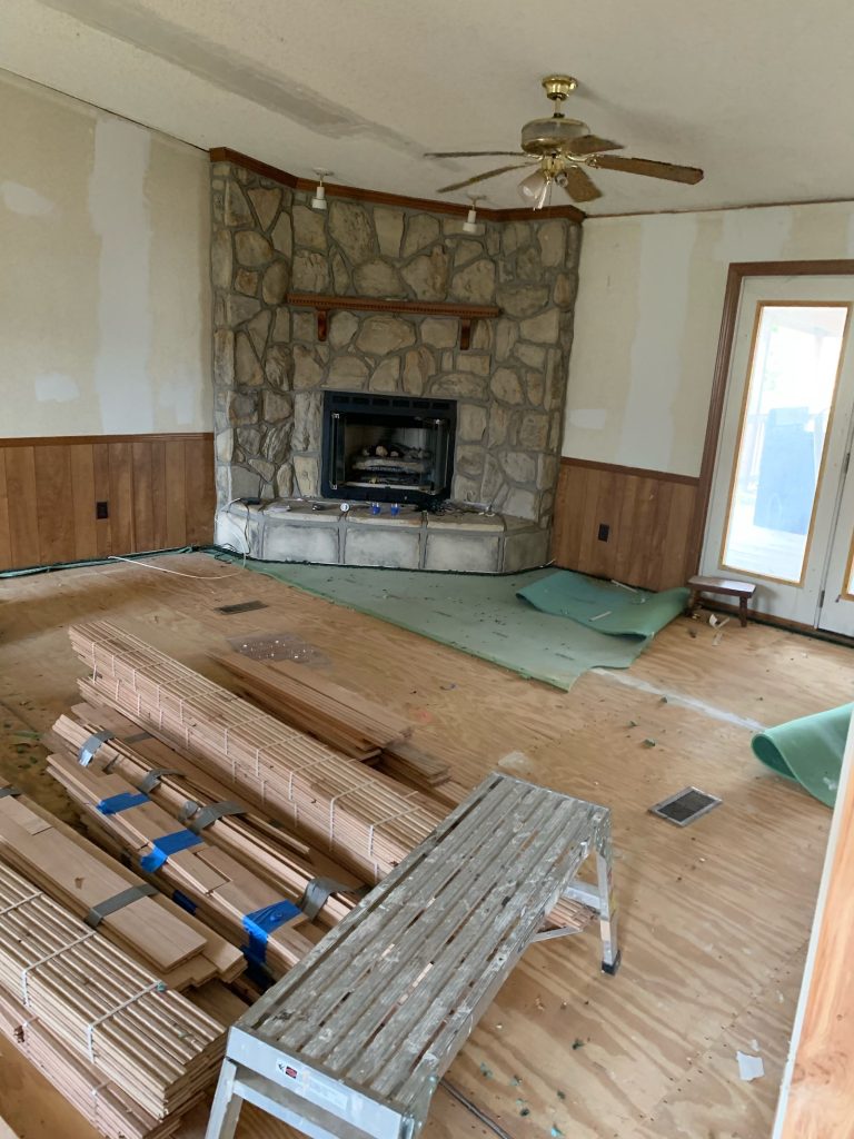 Living room renovation with flooring materials stacked near the stone fireplace