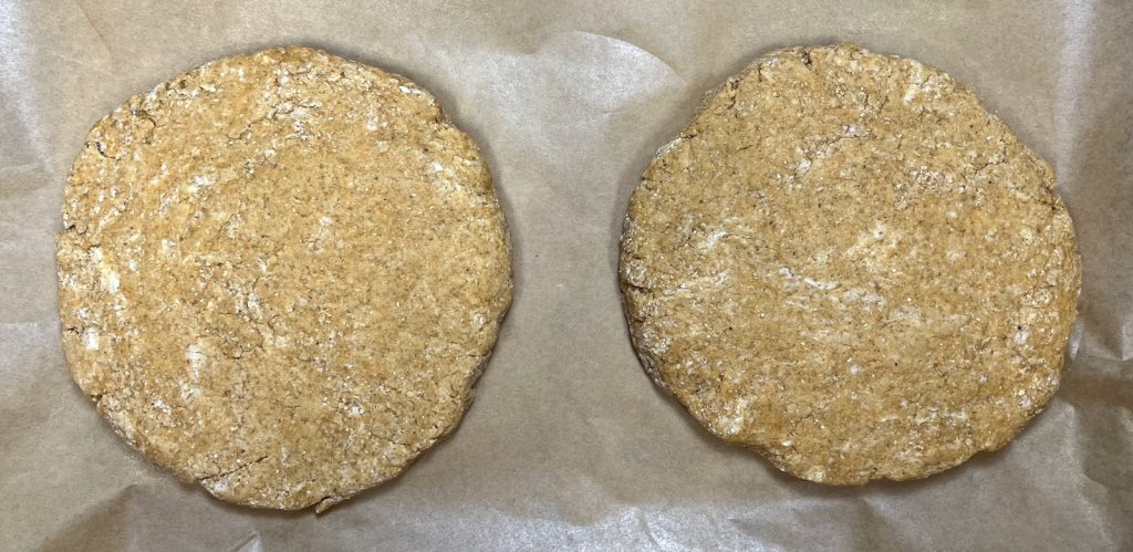 Two rounds of pumpkin sourdough scone dough shaped on parchment paper.