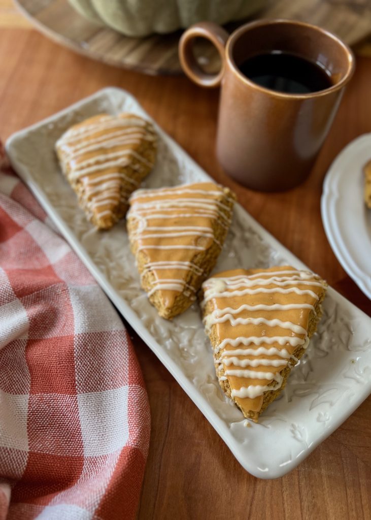 Pumpkin sourdough scones with maple icing served beside coffee and a rust-colored checkered cloth.
