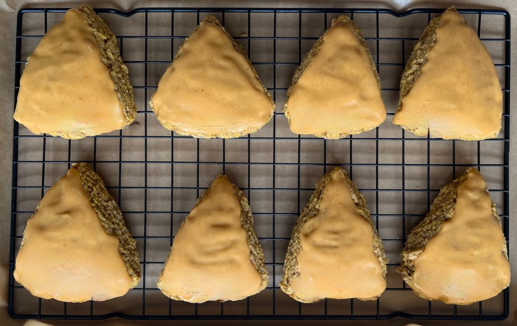 Pumpkin sourdough scones coated with thick pumpkin-maple icing on a cooling rack.
