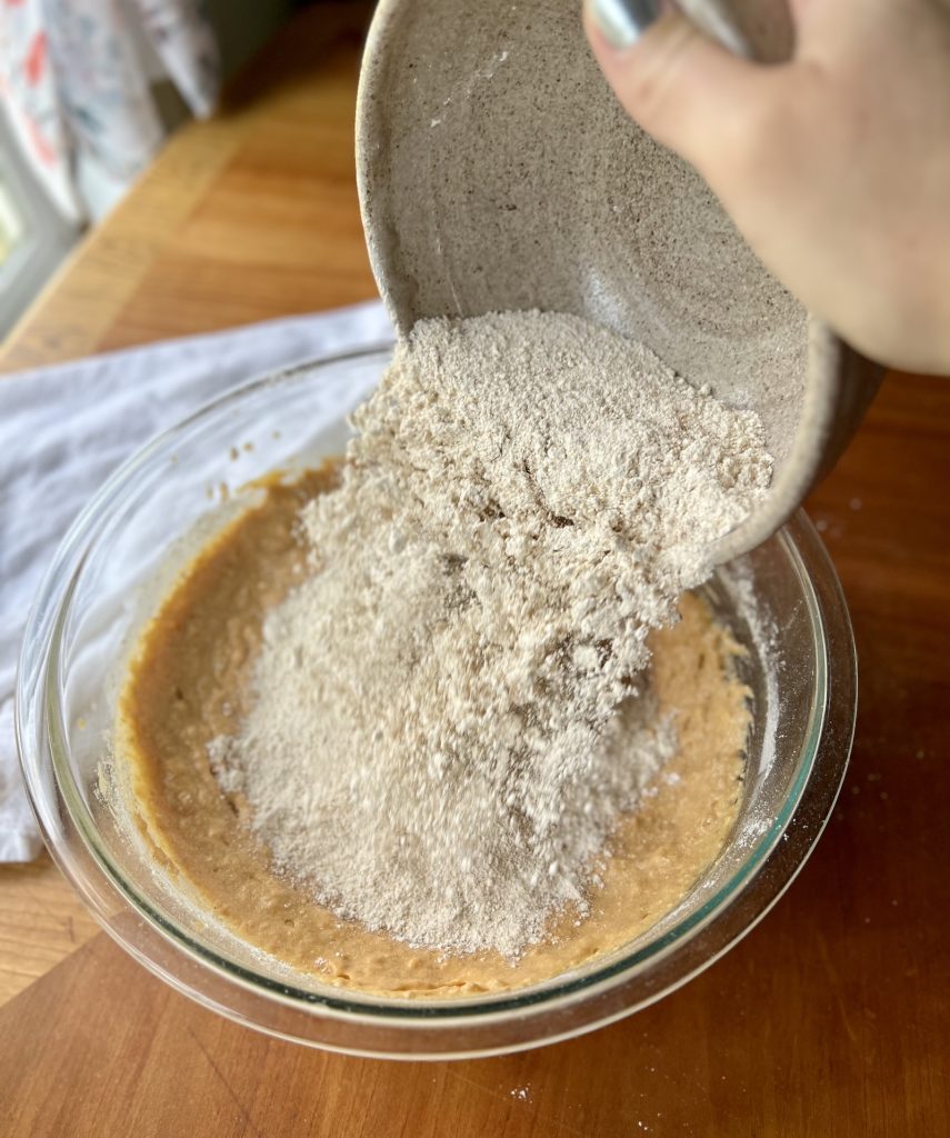 Fresh-milled soft white wheat flour being added to pumpkin muffin batter.