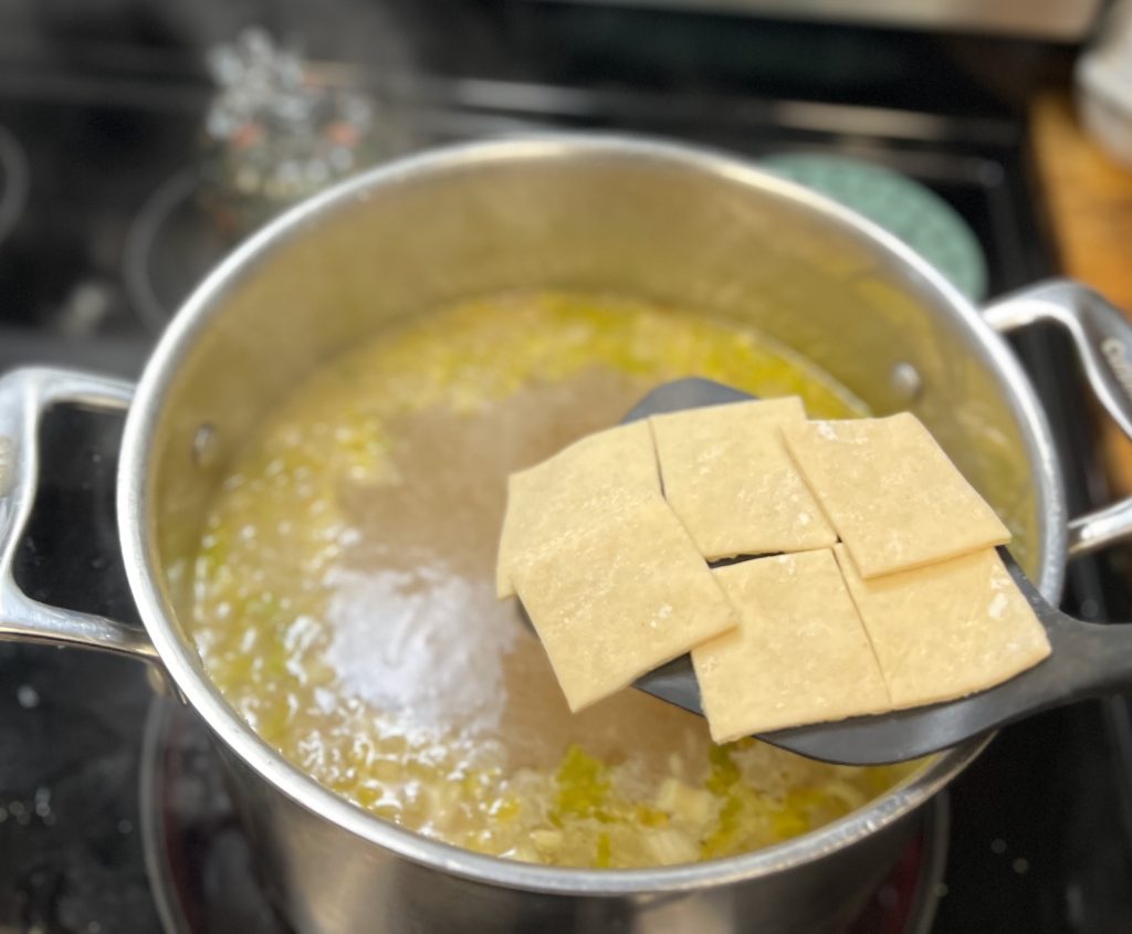 Homemade rolled dumplings being added to simmering chicken broth