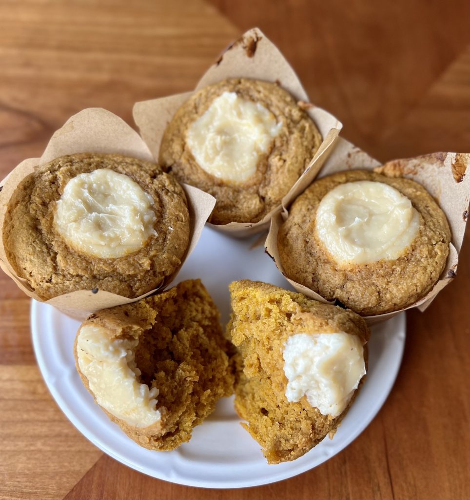 Fresh-milled pumpkin muffins with baked cream cheese topping and one muffin broken open