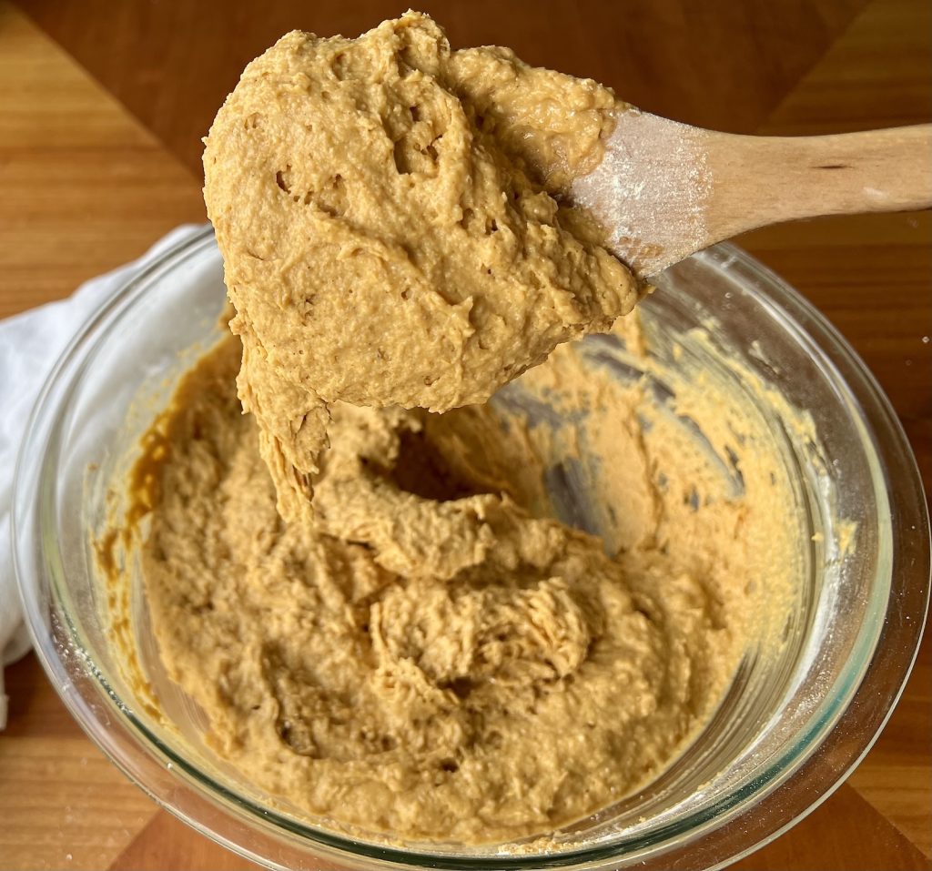 Thick, scoopable fresh-milled pumpkin muffin batter lifted above a glass mixing bowl