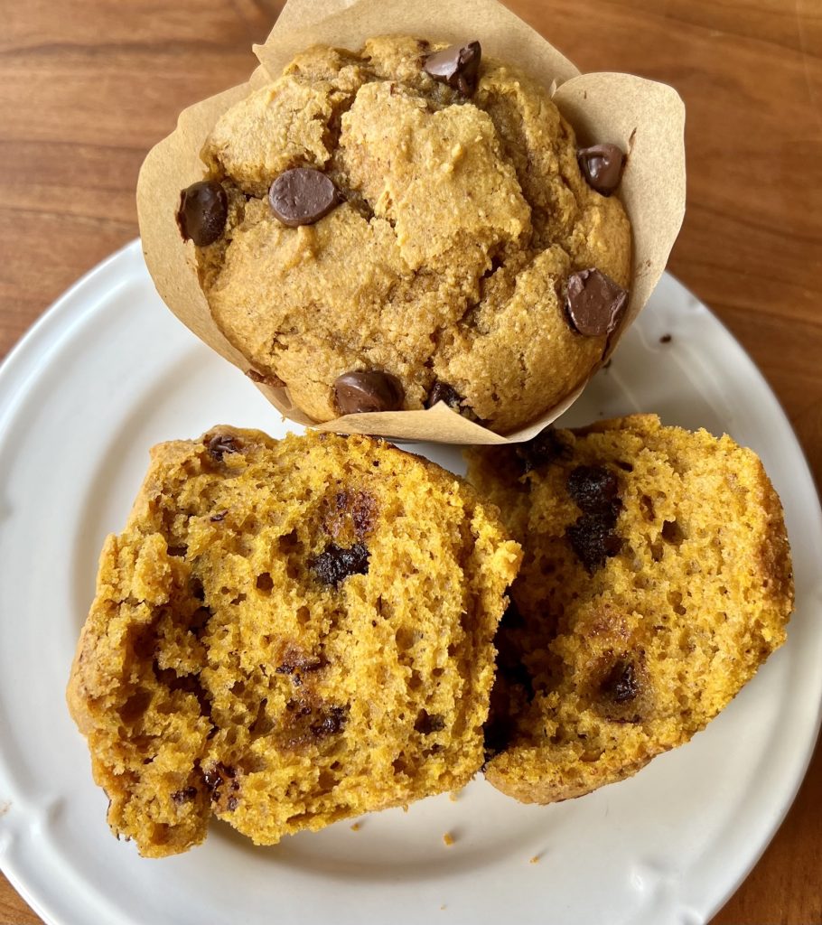 Moist orange pumpkin muffin crumb with melted chocolate chips beside a whole muffin