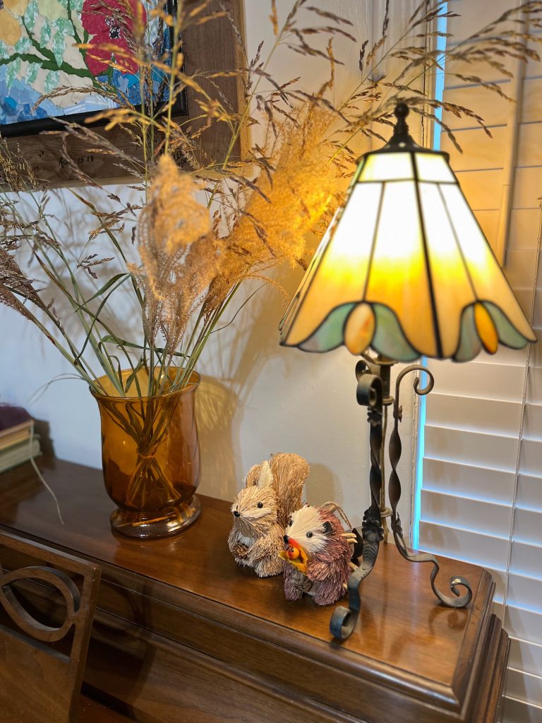 A wooden piano styled with old books, woodland creatures, a glowing lamp and gathered grasses