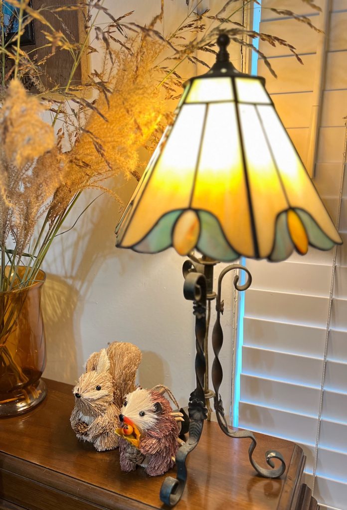 A wooden piano styled with old books, woodland creatures, a glowing lamp and gathered grasses