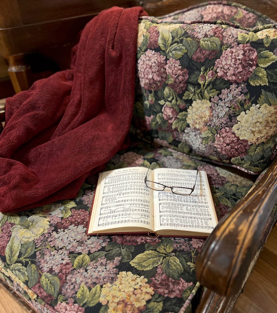 A floral reading chair with a burgundy throw and an old book.
