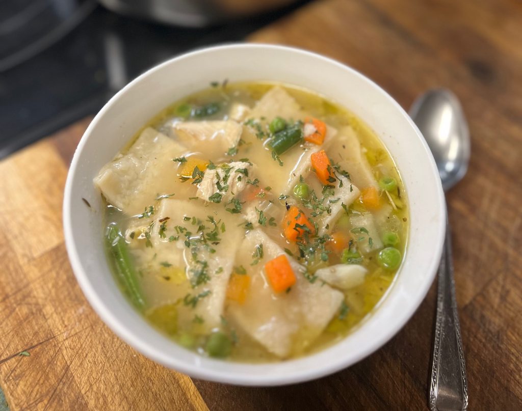 A bowl of steamy Chicken and Dumplings with a big full pot in the background