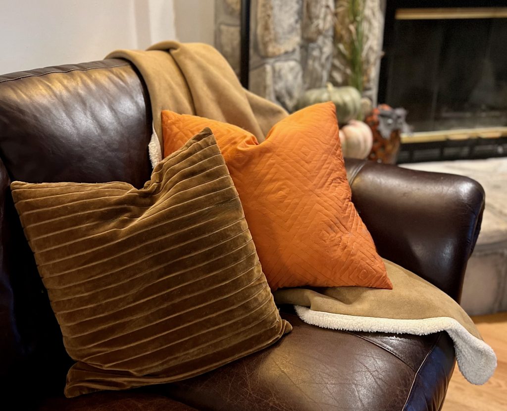 Tan and Cream throw draped over a dark leather sofa with muted orange and brown textured pillows