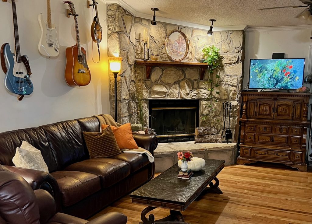 A cozy fall living room with soft blankets and textured pillows, pumpkins, books, and collected grasses from outside.