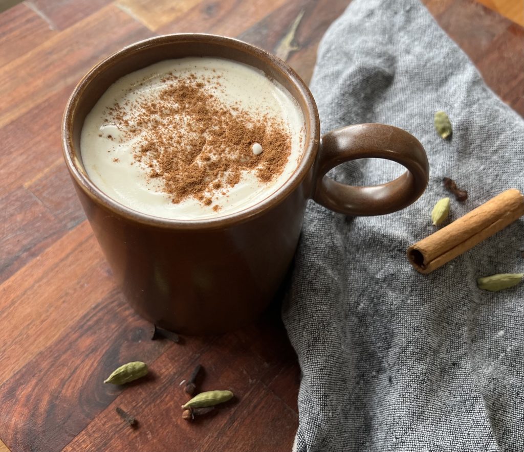 Pumpkin chai tea latte topped with maple whipped cream and cinnamon in a brown mug beside whole spices.