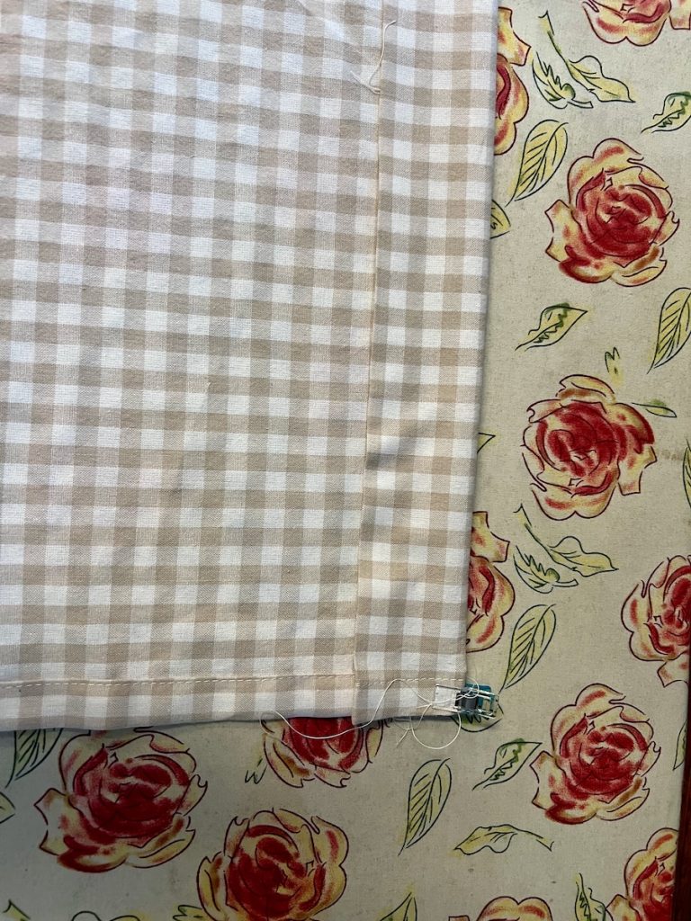 Folded beige gingham fabric prepared for sewing a café curtain rod pocket.