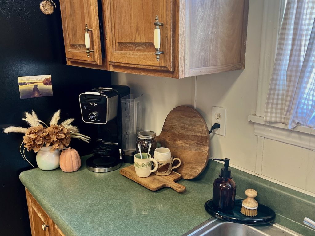 A cozy fall coffee corner with a Ninja coffee maker, dried flowers, wood boards and a green countertop.