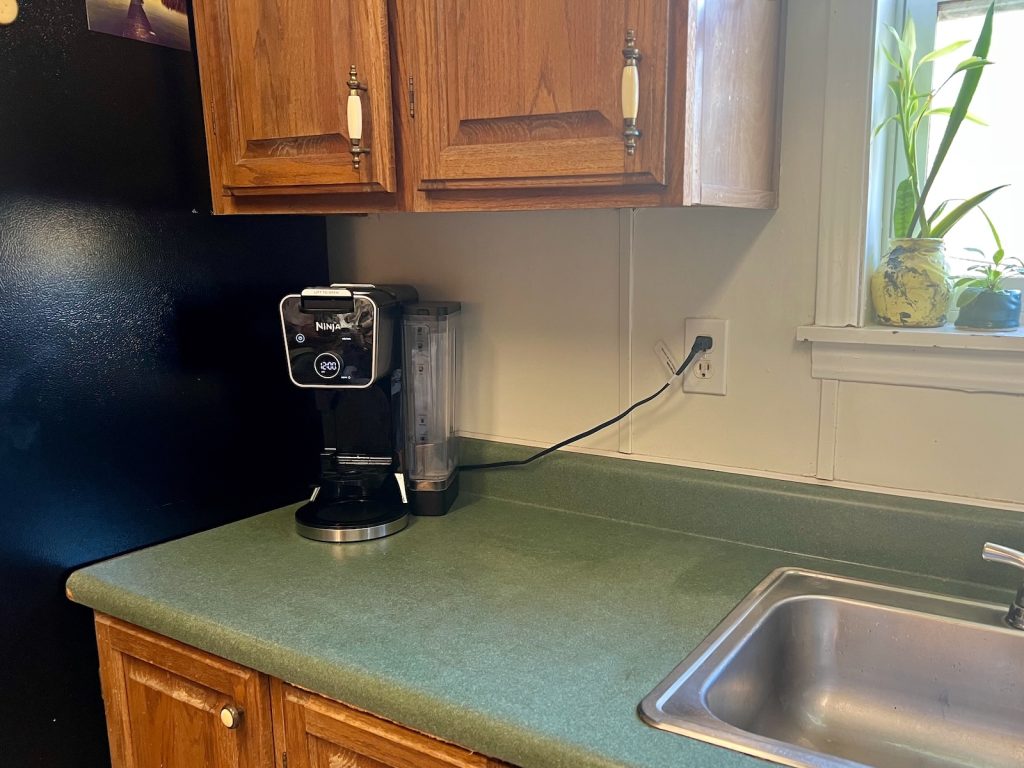 Kitchen coffee corner before decorating, with oak cabinets, green countertops, and a black Ninja coffee maker.