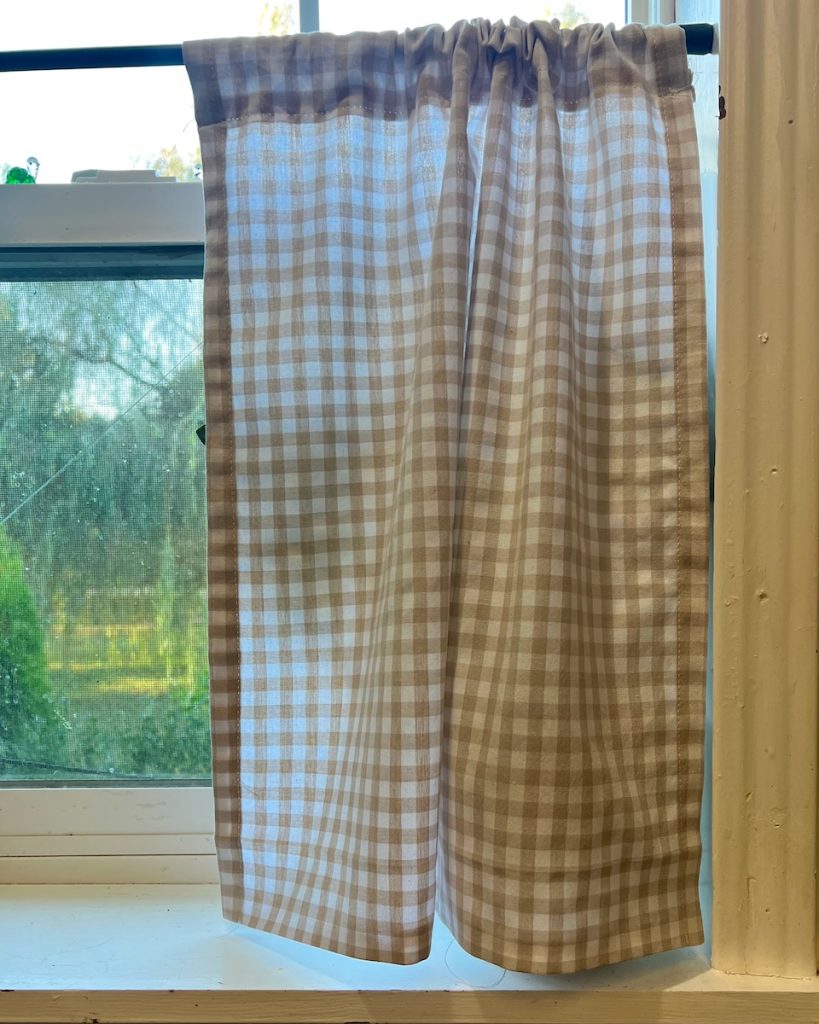 Close-up of the checkered curtain gathered along the rod and hung in the window.