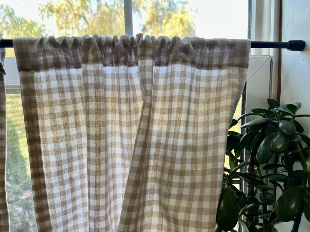 Finished rod pocket on a DIY beige gingham café curtain hanging from a black tension rod.