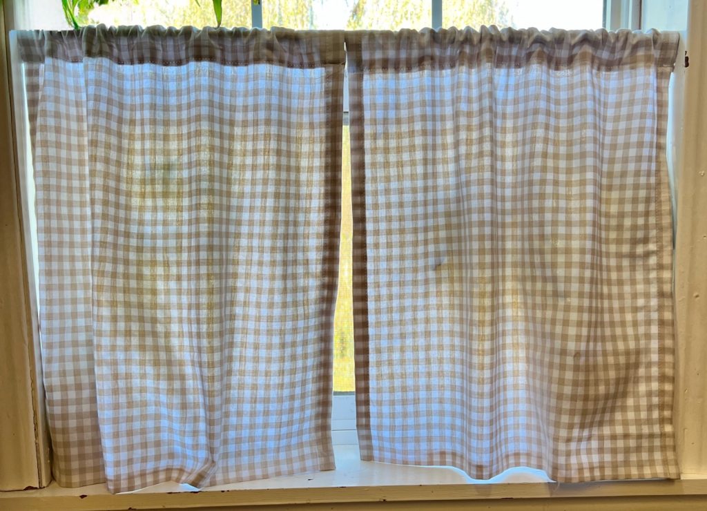 Two finished DIY gingham café curtains hung on a tension rod and hung in the window.