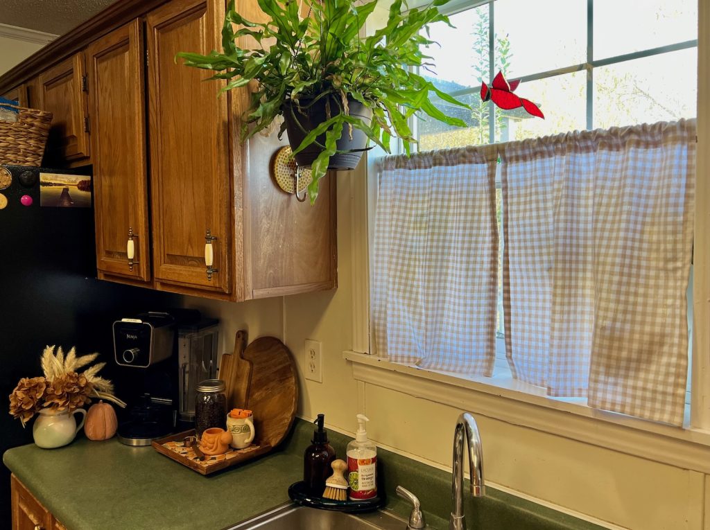 Homemade beige gingham café curtains hanging above a kitchen sink beside my cozy fall home café corner with wooden cutting boards and dried hydrangeas.