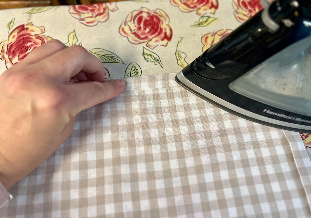 Folding and pressing the edge of a curtain panel with an iron before stitching. 