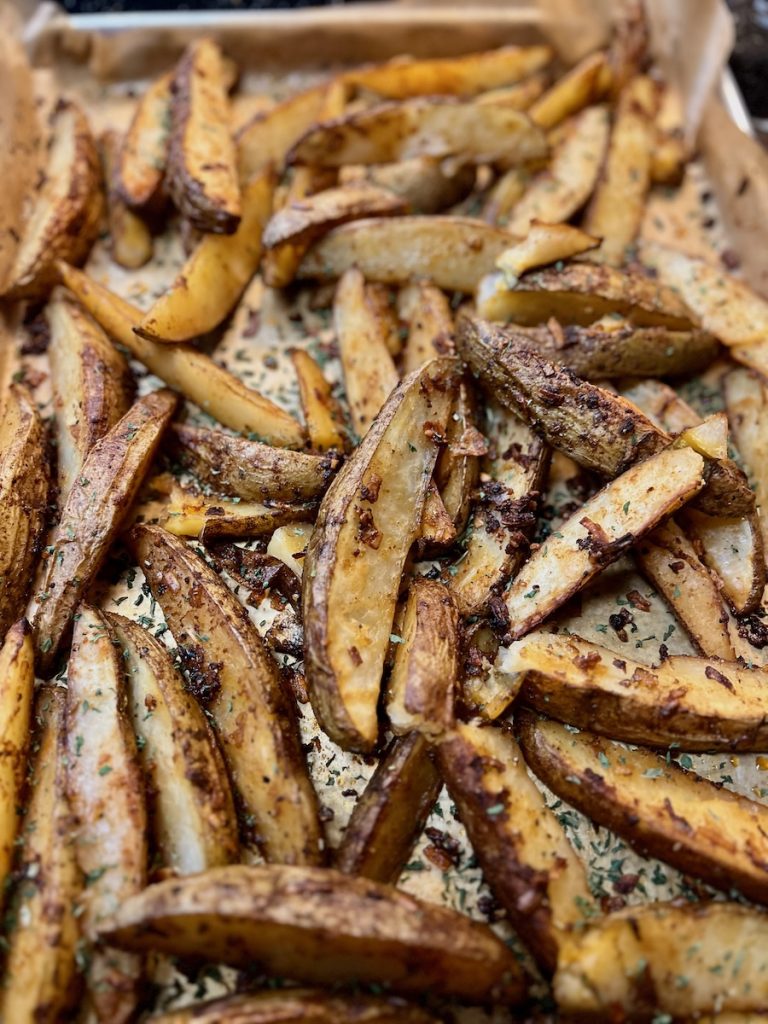 Golden roasted potato wedges with herbs and browned edges on a parchment-lined baking sheet