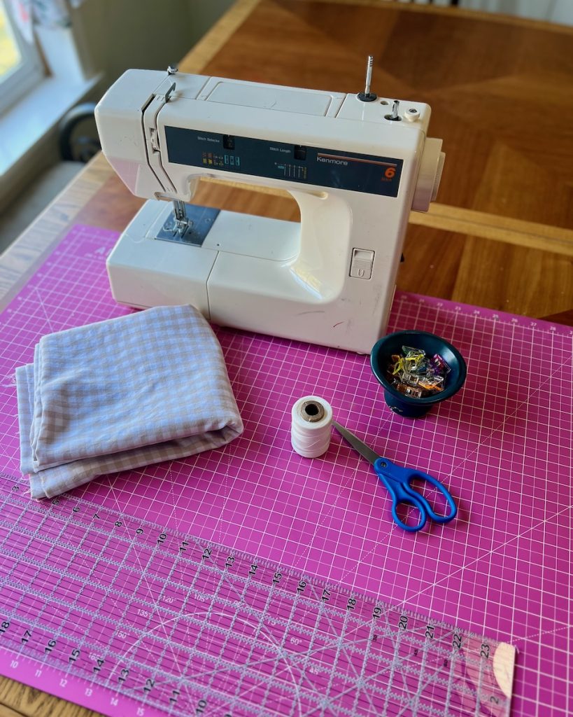 Kenmore sewing machine with gingham fabric, thread, scissors, and sewing clips arranged for a DIY café curtain tutorial