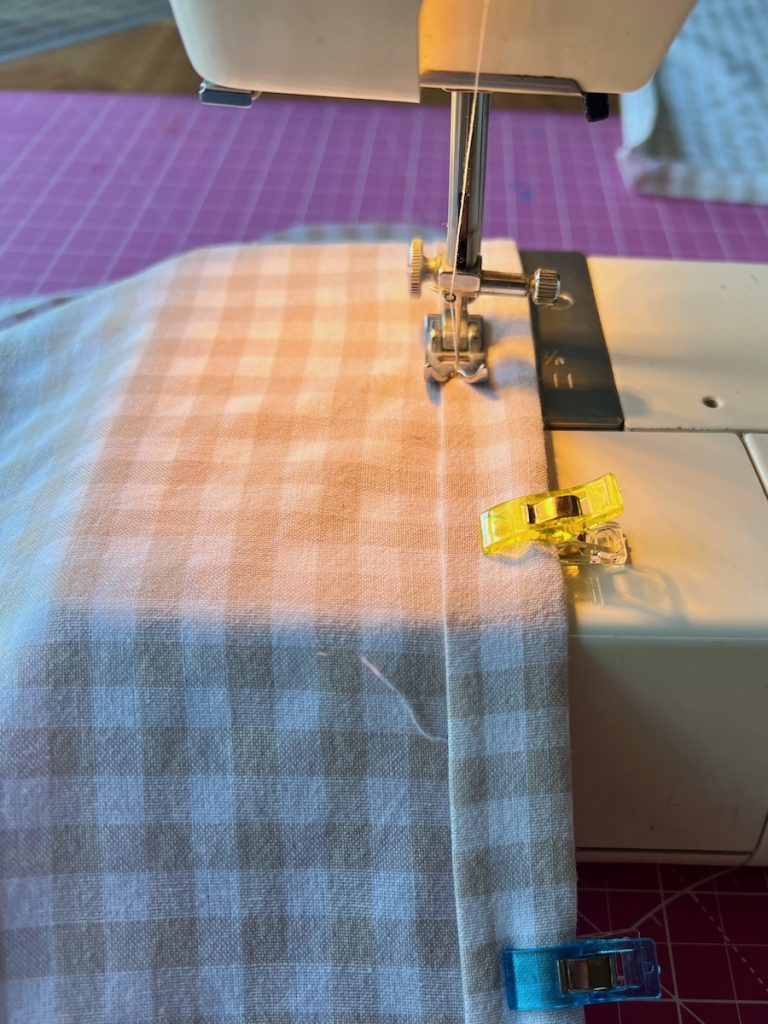 Sewing a straight seam along the folded hem of a beige gingham café curtain edge.