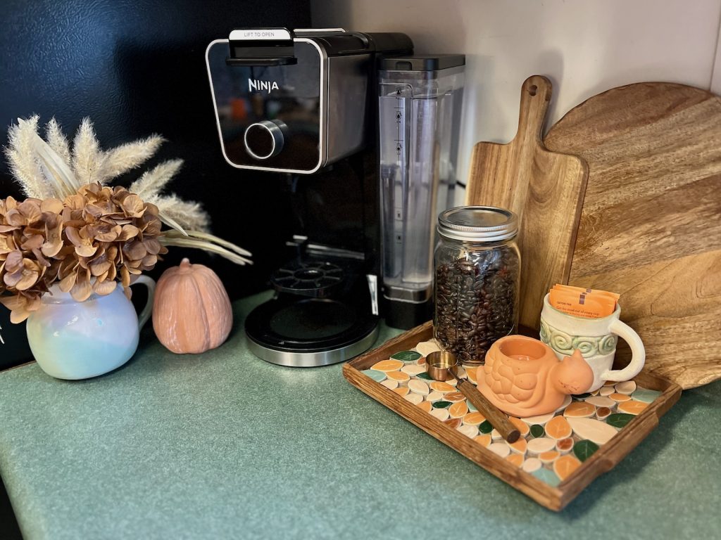 A small fall coffee station decorated with dried hydrangeas, a clay pumpkin and a tray of coffee supplies